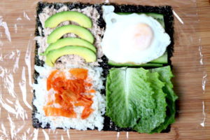 Unterschiedliche Zutaten, wie Reis, Kimchi, Thunfisch, Avocado, Spiegelei und Salat, gleichmäßig auf den vier Feldern des Seetangblattes verteilen.